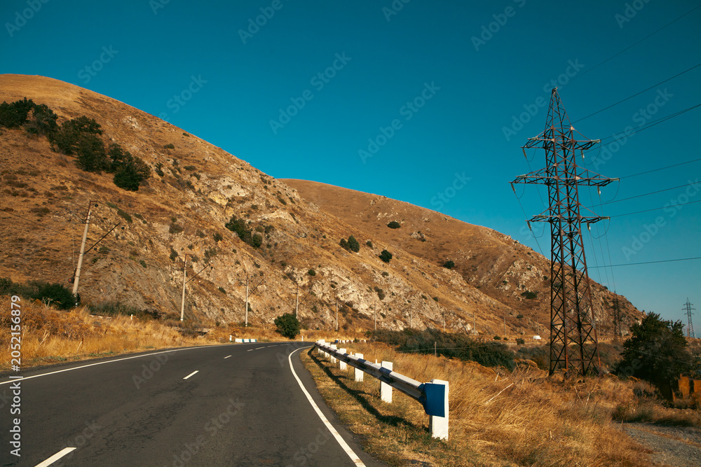 Obraz premium Highway in the mountains with clear blue sky and white clouds.