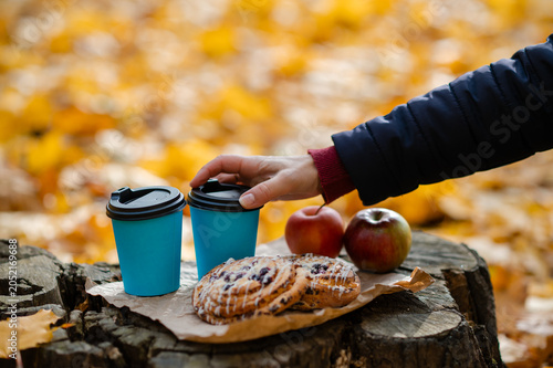 Autumn picnic concept - female hand reaching for cup on tree stump with pastries and apples among colorful leaves