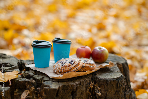 Autumn picnic concept - cups, pastries, and apples on old tree stump among colorful leaves