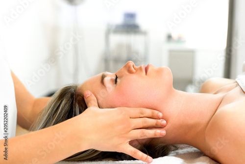 Relaxed woman receiving gentle neck and jaw massage in bright treatment room