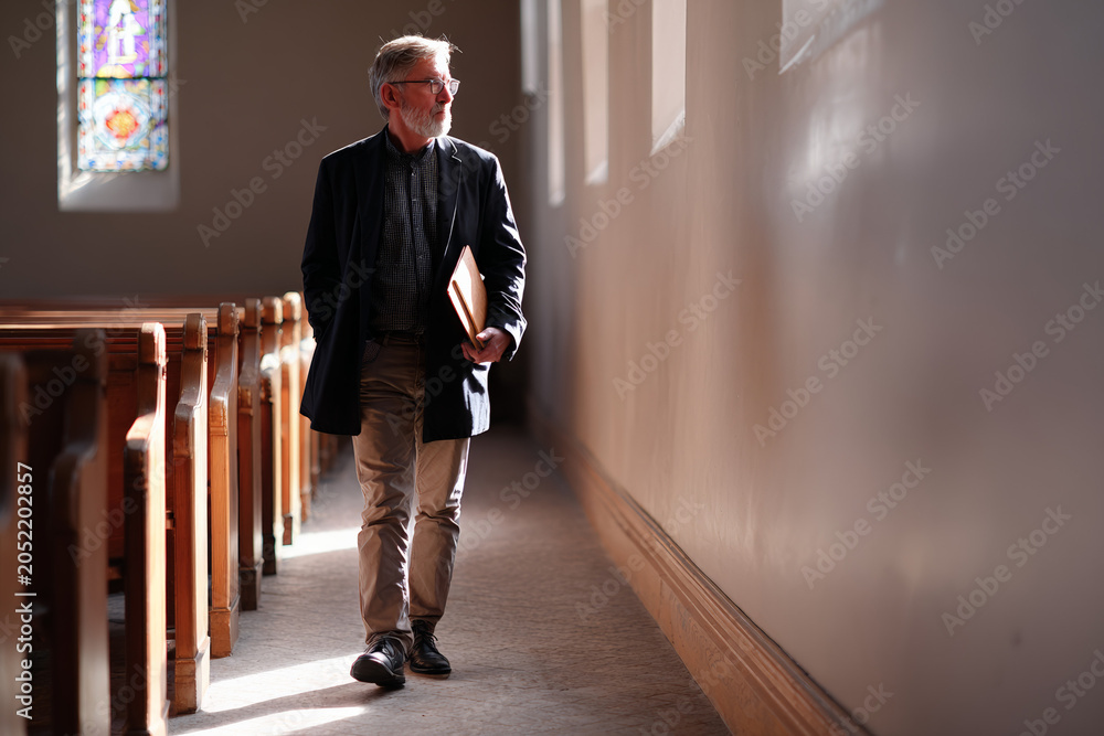 Obraz premium Elderly man walking with folder along church aisle interior