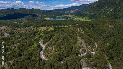 drone perspective of the winding curves of the SH75 scenic mountain pass road cutting through a lush green pine forest in Albania