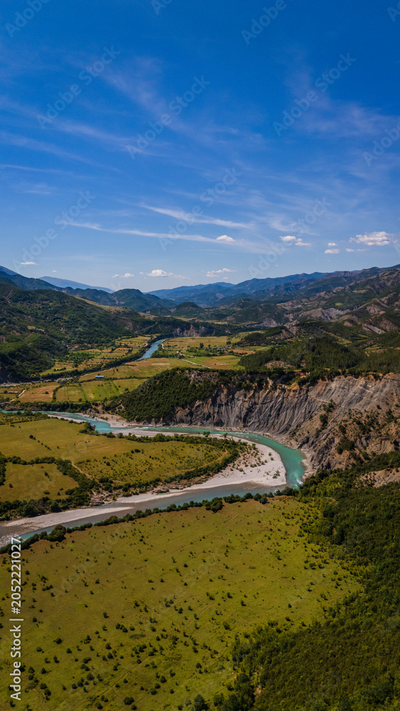 Fototapeta premium drone view showcasing the sweeping curves of the Vjosa river beneath the majestic Nemërçka mountain peaks near Këlcyrë, Albania