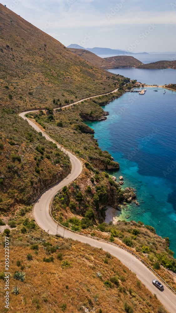 Fototapeta premium Aerial drone perspective of the scenic SH8 coastal highway winding along the steep mountain ridges of the Albanian Riviera. Breathtaking Mediterranean landscape