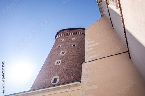 Tower rises against blue sky in city with brick walls and clear sunlight during daytime with buildings around it. Wawel castle, Krakow, Poland