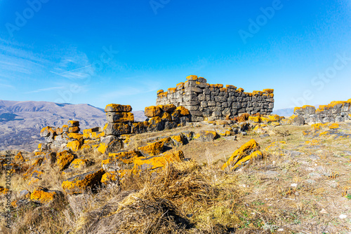 A wall of large gray stones from an old fortress, megaliths covered in bright brown lichen. Hills, mountains, and the sky in the background. Saro, Meskheti, Javakheti, Georgia.