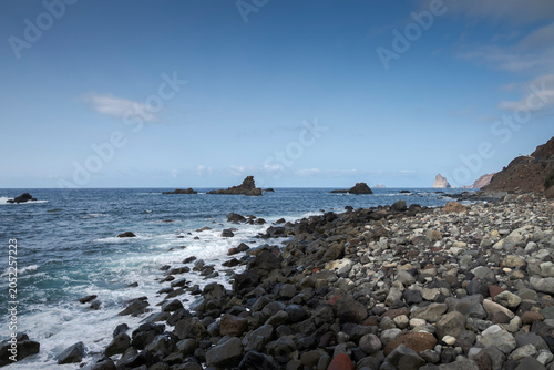 Rocky beach on the north coast of Tenerife, Canary Islands, Spain, at Almaciga beach, with dark volcanic stones, blue ocean waves, and a clear sky.