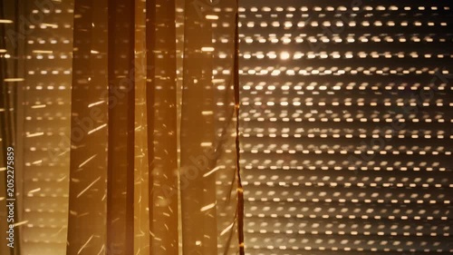 Warm golden sunlight streams through closed window blinds, creating dotted patterns and dramatic shadows across a curtain and interior surfaces, 4K