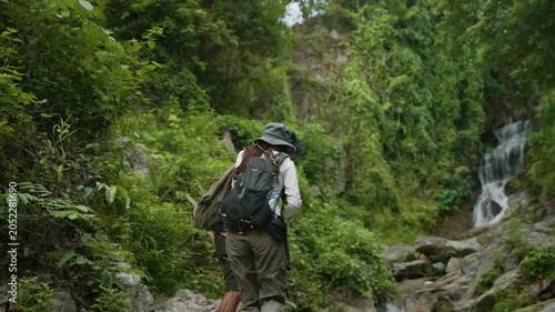 Romantic young couple holding hands while hiking together in a lush green jungle towards a waterfall