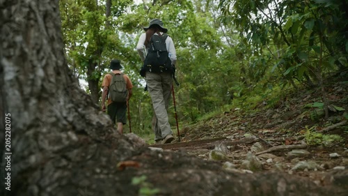 Young couple hiking up a rocky trail through a lush green forest with backpacks and trekking poles