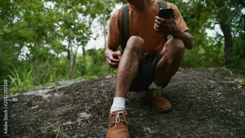 Adventurous young man using a smartphone for navigation while taking a break during a hike in a lush green forest