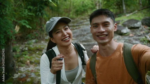 Asian couple hiking in a tropical forest live streaming their adventure with a selfie stick