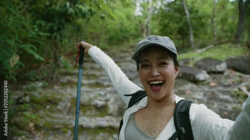 Asian woman having a video call while hiking and vlogging her adventure in a lush green forest