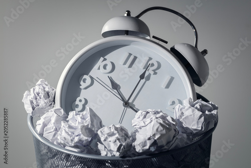 Wasting time, procrastination, delay or being unproductive, alarm clock in a wastepaper bin