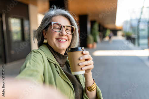Foto Mature woman enjoying a coffee break in the city, smiling and taking a cheerful