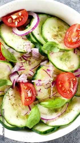 macro shot of a fresh cucumber salad with cherry tomatoes red onion and basil leaves in a white bowl