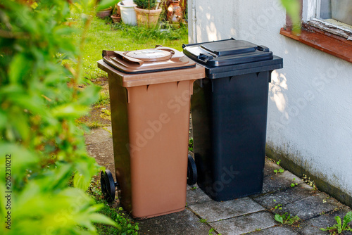 Brown bio waste bin and black residual waste bin standing side by side for recycling in a backyard.