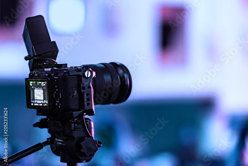 Professional camera on tripod recording a seminar with blurred audience in background. Videography equipment