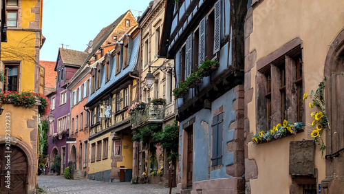 Foto Colorful half timbered houses along a winding cobblestone street in a historic Alsace village of Riquewihr, blending French charm, preserved architecture and inviting old town travel atmosphere