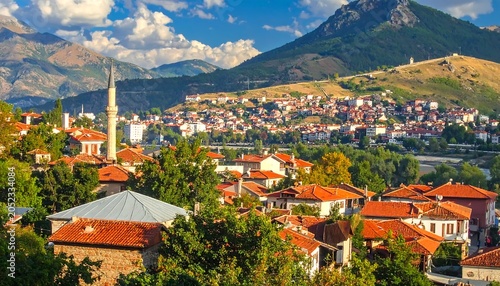 Scenic vista of a town nestled amidst mountains, featuring red-tiled roofs, a tall minaret, and lush greenery