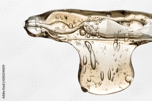 Yellow cosmetic gel with bubbles flows from a glass pipette, a product for facial and hand care.