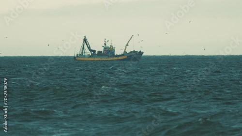 Fishermen work on a boat in the ocean while birds fly around in the distance during the late afternoon