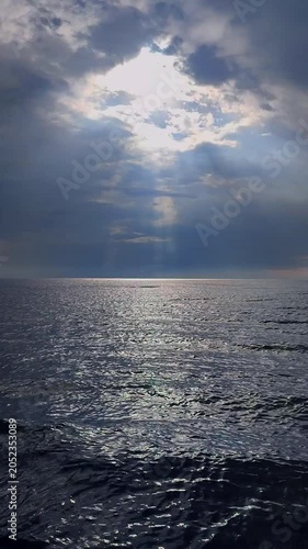 Rain in sea. Rain falling in sea. Cloudy, rainy, stormy weather at sea. Dark rainy clouds over water. Sea, sky, clouds and horizon line. Seascape. Landscape. The sun shining through clouds Vertical