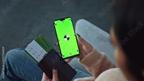 Focused Unrecognizable Woman Holding Smartphone With Green Screen And Travel Document In Hand, Sitting On Couch In Modern Living Room. Technology And Travel Lifestyle Concept.