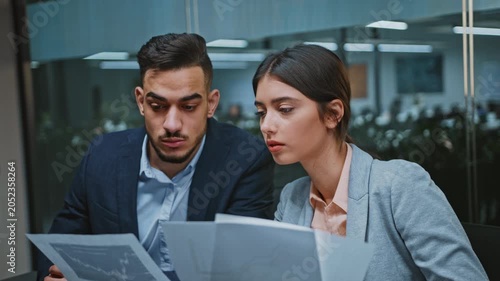 Focused Expressions. Young Businessman And Businesswoman Collaborating On Project Together In Modern Office Setting, Analyzing Documents And Discussing Ideas. Business Concept.