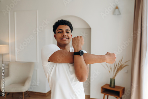 Bild auf Leinwand Young African American man in white t-shirt stretches arms inside a modern livin
