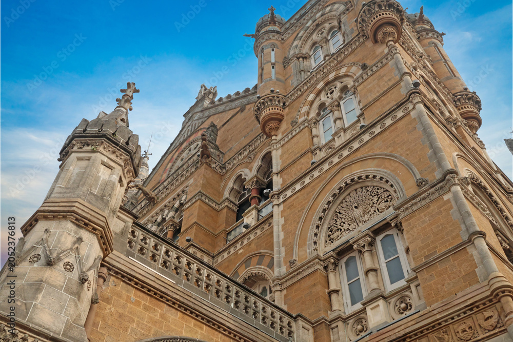 Fototapeta premium Mumbai Maharashtra India Jan 18 2026 Low angle architectural view of the ornate stone facade and soaring towers of Chhatrapati Shivaji Maharaj Terminus against a clear blue sky.