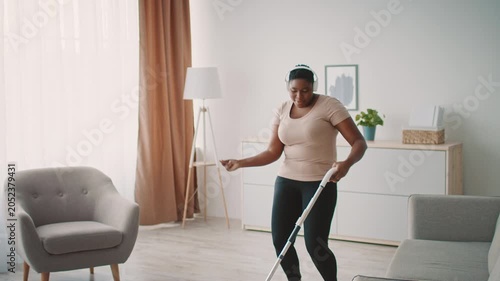 Smiling Black Woman Enjoying Cleaning Living Room While Using Vacuum Cleaner At Home. Radiating Happiness While Engaged In Household Chores In A Cozy Living Space. Weight Loss Concept.