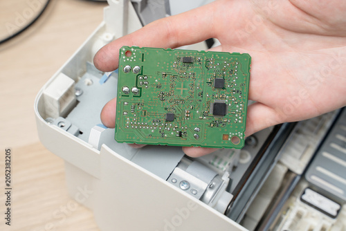 Hand Holding Green Circuit Board Inside Disassembled Printer During Electronics Repair And Maintenance
