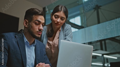 Focused Young Man And Woman Working Together At Laptop In Modern Office Environment, Engaged In Discussion And Collaboration While Analyzing Information, Business Concept.