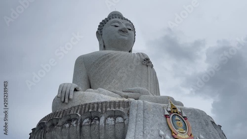 Low-angle view of the iconic Big Buddha statue in Phuket, Thailand, under dramatic cloudy skies. A landmark Buddhist monument and major cultural attraction on the island