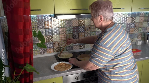 Grandmother frying thin pancakes in a frying pan. Senior woman cooking on the stove