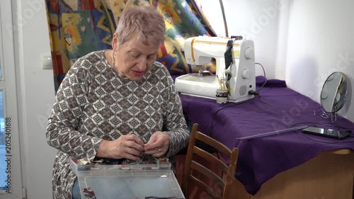 Senior elderly woman is engaged in needlework. She lays out scraps for sewing. Grandmother craft at home
