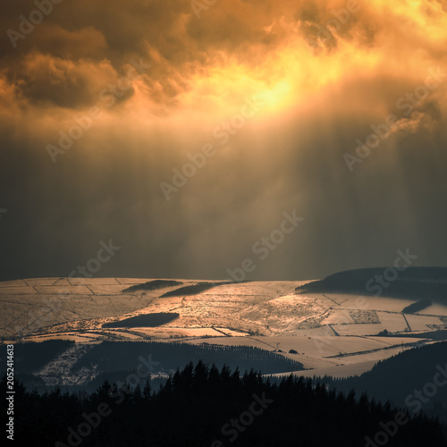 Sunbeams filter through the clouds and tinge with gold the snowy hills
