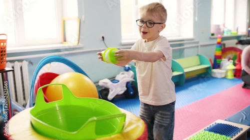 Woman helps a young boy navigate colorful blocks in a vibrant children's playroom, surrounded by various toys and educational items