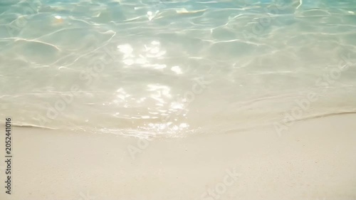 Clear water shoreline, sandy beach, sunlight ripple, gentle wave, pale sand, calm shore with sea water reflection