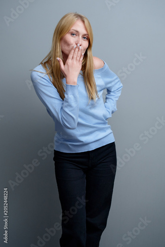 Картината върху платно Smiling Woman in Blue Sweater Making a Playful Gesture on Gray Background
