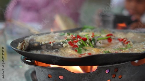 4K Close-up Thai steamed fish with chili and garlic on hot fish-shaped stove boiling with steam, Spicy local food traditional culinary.