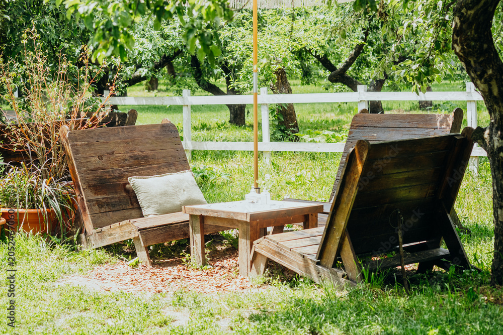 Fototapeta premium Wooden chairs and table in a garden under fruit trees