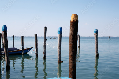 Foto Wooden mooring poles and boat on the water, Pellestrina, Italy