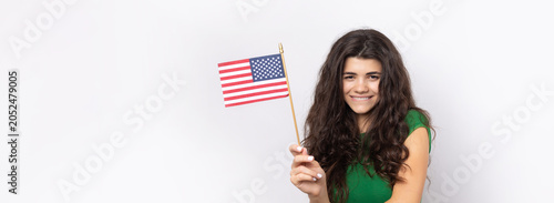 A young happy girl with a smile on her face holds an American flag in her hands. Symbol of patriotism and freedom.
