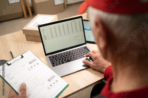 Male warehouse worker using laptop computer with open software on workspace working in e-commerce and small business. Online shop