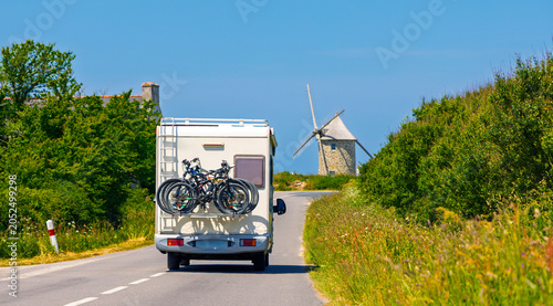 Valokuva Motorhome driving on a countryside road toward a traditional windmill, France -