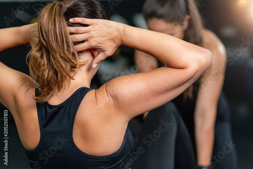 Bild auf Leinwand Woman performs a sit-up repetition with hands clasped behind her head, captured from behind showing engaged back and arm muscles during a core strengthening workout in a gym