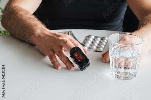 Foto Mature man measures his blood oxygen with a fingertip pulse oximeter beside pills and a glass of water illustrating home health monitoring and preventive self care