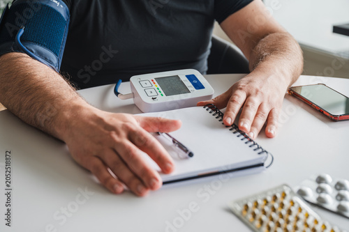Tableau sur toile Vertical photo of a mature man with an arm cuff reading his digital home blood pressure monitor at a table illustrating hypertension self-monitoring heart health and preventive home healthcare